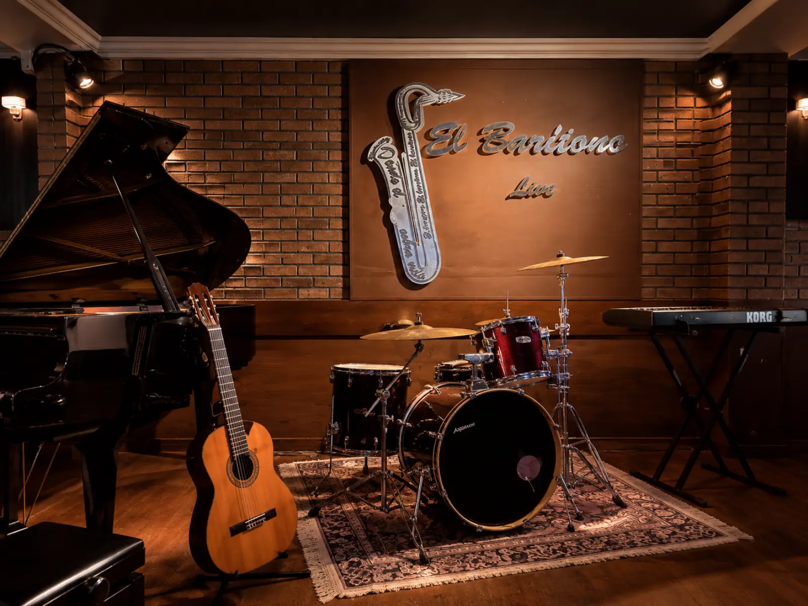 Escenario con piano, batería y letrero El Barítono Live sobre pared de ladrillo